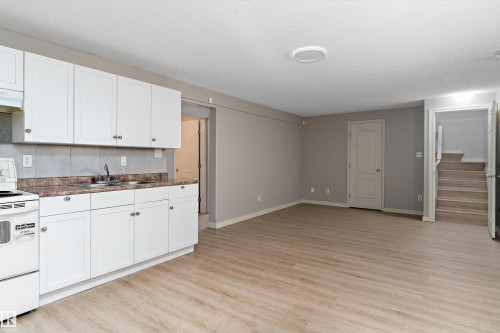 Kitchenette featuring white cabinetry, a double basin sink, and a white electric range - 15109 Miller Boulevard, Edmonton, AB - Indoor Photo Showing Kitchen With Double Sink