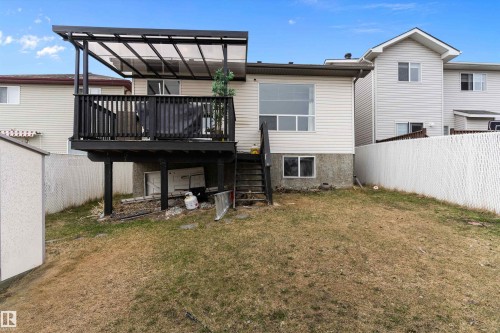 Back exterior featuring a black elevated wood deck with a clear panel awning, white vinyl siding, and a white chain-link fence bordering the property - 15109 Miller Boulevard, Edmonton, AB - Outdoor With Deck Patio Veranda With Exterior