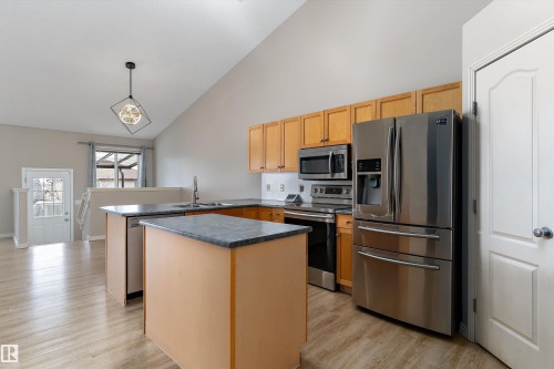 Kitchen featuring stainless steel appliances, wood cabinetry, an island with countertop, and wood-finish flooring - 15109 Miller Boulevard, Edmonton, AB - Indoor Photo Showing Kitchen With Stainless Steel Kitchen With Double Sink