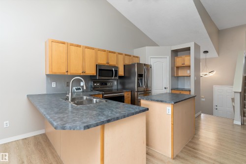 Kitchen featuring wood-finish cabinetry, stainless steel appliances, and a double basin sink - 15109 Miller Boulevard, Edmonton, AB - Indoor Photo Showing Kitchen With Double Sink
