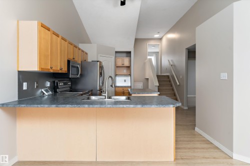 Kitchen featuring light wood cabinetry, a stainless steel sink with a high-arc faucet, dark countertops, and stainless steel appliances - 15109 Miller Boulevard, Edmonton, AB - Indoor Photo Showing Kitchen