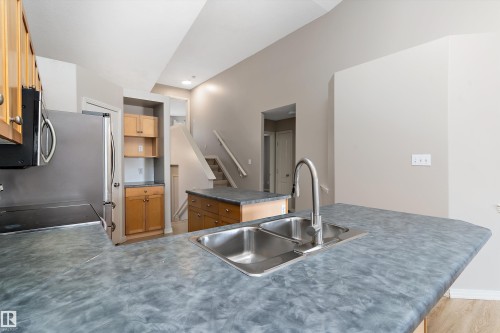 Kitchen featuring a double stainless steel sink with a high-arc faucet, durable countertops, wood-finish cabinetry, and stainless steel appliances - 15109 Miller Boulevard, Edmonton, AB - Indoor Photo Showing Kitchen With Double Sink