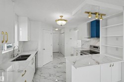 Open-concept kitchen featuring marble-look flooring and countertops, white cabinetry with gold-tone hardware, a stainless steel electric range, and a blue range hood - 