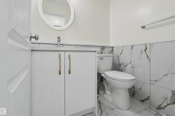 Bathroom featuring a single-sink vanity with white cabinetry, gold-tone hardware, and a round wall mirror - 