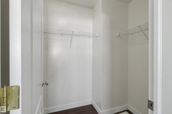 Walk-in closet with dark wood-finish flooring, white baseboards, and two levels of wire shelving - 