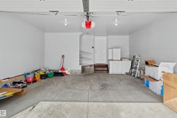 Spacious garage featuring a concrete floor, painted white walls, built-in shelving, a service door, and overhead lighting - 