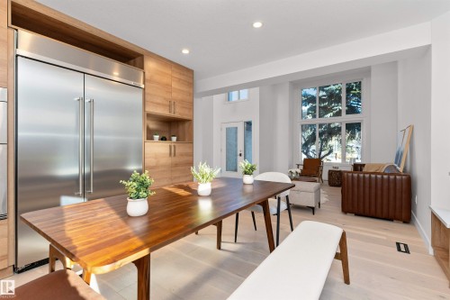 Open-concept living area featuring light wood-finish flooring, a stainless steel refrigerator, wood cabinetry, recessed lighting, and large windows - 607 Butterworth Wynd, Edmonton, AB - Indoor