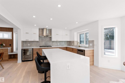 Bright kitchen featuring a large center island with integrated seating, stainless steel appliances, white upper cabinetry, wood-finish lower cabinetry, and a beverage cooler - 607 Butterworth Wynd, Edmonton, AB - Indoor Photo Showing Kitchen With Upgraded Kitchen