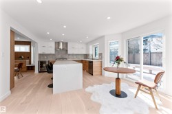 Open-concept kitchen featuring light wood-finish flooring, white cabinetry, a large kitchen island, stainless steel appliances, and a sliding glass door to the exterior - 