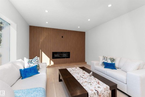 Living area featuring a wood-finish accent wall with an integrated linear fireplace, light wood-finish flooring, and recessed ceiling lighting - 607 Butterworth Wynd, Edmonton, AB - Indoor Photo Showing Living Room With Fireplace