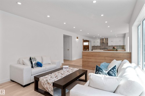 Open-concept living area featuring light wood-finish flooring, recessed ceiling lighting, a large window, and a kitchen with white cabinetry and a stainless steel range hood - 607 Butterworth Wynd, Edmonton, AB - Indoor Photo Showing Living Room