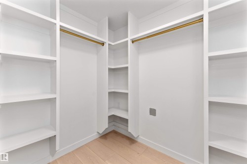Custom closet system with white shelving, integrated hanging rods, corner shelving units, and light wood-finish flooring - 607 Butterworth Wynd, Edmonton, AB - Indoor With Storage