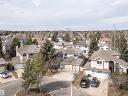 Residential streetscape featuring a collection of multi-story homes with attached garages, mature trees, and varied roofing materials - 