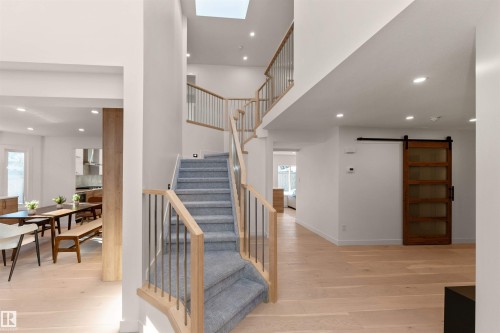 Open-concept main level featuring light wood-finish flooring, a contemporary staircase with carpeted treads and metal balusters, a skylight, recessed lighting, and a modern barn door with frosted glass panels - 607 Butterworth Wynd, Edmonton, AB - Indoor Photo Showing Other Room