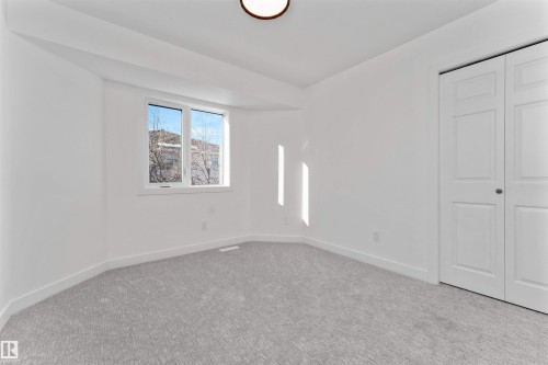 Bright room featuring a large window, neutral gray carpet, white baseboards, and a bi-fold closet door - 607 Butterworth Wynd, Edmonton, AB - Indoor Photo Showing Other Room