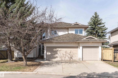 Two-story stucco exterior featuring a two-car garage with individual doors, a concrete driveway, and mature trees - 607 Butterworth Wynd, Edmonton, AB - Outdoor