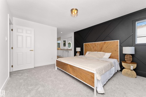 Spacious bedroom featuring light grey carpeting, a prominent black accent wall with geometric paneling, and a single window with white trim - 607 Butterworth Wynd, Edmonton, AB - Indoor Photo Showing Bedroom