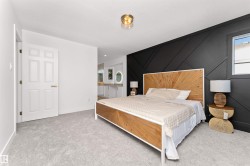 Spacious bedroom featuring light grey carpeting, a prominent black accent wall with geometric paneling, and a single window with white trim - 
