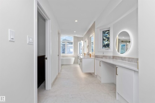 Spacious bathroom featuring a freestanding tub, dual floating vanities with gold-tone fixtures, a backlit oval mirror, and a makeup vanity with quartz countertops - 607 Butterworth Wynd, Edmonton, AB - Indoor Photo Showing Other Room