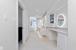 Spacious bathroom featuring a freestanding tub, dual floating vanities with gold-tone fixtures, a backlit oval mirror, and a makeup vanity with quartz countertops - 