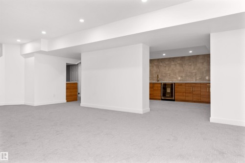 Spacious finished area featuring light gray carpeting, recessed ceiling lighting, a built-in wet bar with wood cabinetry, a beverage refrigerator, and a stainless steel sink - 607 Butterworth Wynd, Edmonton, AB - Indoor Photo Showing Other Room