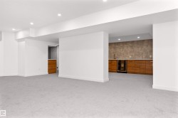 Spacious finished area featuring light gray carpeting, recessed ceiling lighting, a built-in wet bar with wood cabinetry, a beverage refrigerator, and a stainless steel sink - 