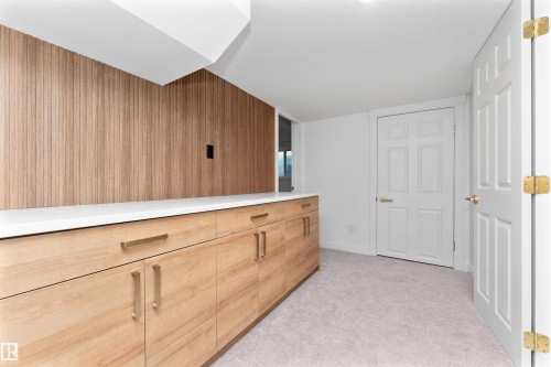 Light wood-finish cabinetry with brass hardware, a white countertop, and a matching wood-finish accent wall - 607 Butterworth Wynd, Edmonton, AB - Indoor Photo Showing Other Room