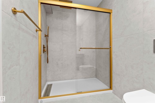 Shower enclosure featuring gold-toned framing, clear glass sliding doors, and a gold-toned shower system with a handheld sprayer - 607 Butterworth Wynd, Edmonton, AB - Indoor Photo Showing Bathroom