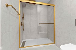 Shower enclosure featuring gold-toned framing, clear glass sliding doors, and a gold-toned shower system with a handheld sprayer - 
