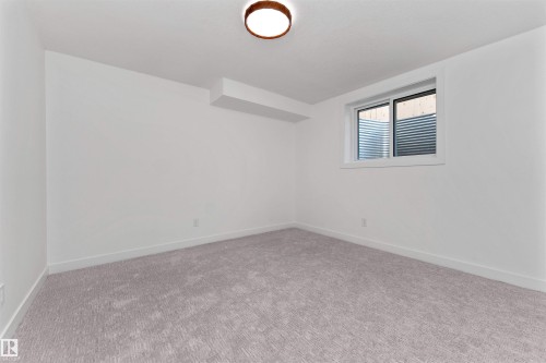 Carpeted room featuring a white ceiling and walls, a window with a window well, a ceiling-mounted light fixture, and white baseboards - 607 Butterworth Wynd, Edmonton, AB - Indoor Photo Showing Other Room