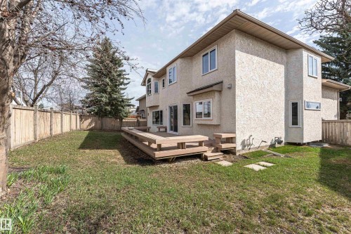 Expansive backyard featuring a large wooden deck with built-in seating, privacy fencing, mature trees, and a stucco exterior with multiple windows - 607 Butterworth Wynd, Edmonton, AB - Outdoor