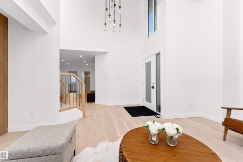 Two-story entry foyer featuring a modern chandelier, light wood-finish flooring, a contemporary staircase with wood handrail and metal spindles, and a glass-paneled entry door with an overhead transom window - 607 Butterworth Wynd, Edmonton, AB - Indoor