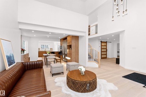 Open concept interior featuring high ceilings, light wood-finish flooring, a contemporary kitchen with stainless steel appliances, a multi-story staircase with metal railings, and a wood barn door - 607 Butterworth Wynd, Edmonton, AB - Indoor Photo Showing Living Room