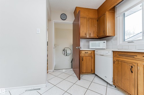 Spacious room featuring a brick fireplace with mantel, exposed brick accent wall with wall-mounted lighting, light-toned carpeting, and white painted walls - 11423 50 Avenue, Edmonton, AB - Indoor Photo Showing Other Room With Fireplace