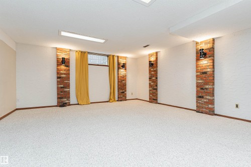 Spacious room featuring light-colored carpeting, white textured walls, and exposed brick columns - 11423 50 Avenue, Edmonton, AB - Indoor Photo Showing Other Room