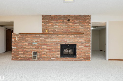 Brick fireplace featuring a black metal firebox and a wooden mantel - 11423 50 Avenue, Edmonton, AB - Indoor Photo Showing Living Room With Fireplace