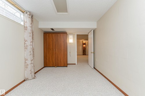 Carpeted room featuring a drop ceiling, a wood-finish armoire, a wall-mounted light fixture, a high horizontal window, and a doorway opening to an interior space - 11423 50 Avenue, Edmonton, AB - Indoor Photo Showing Other Room