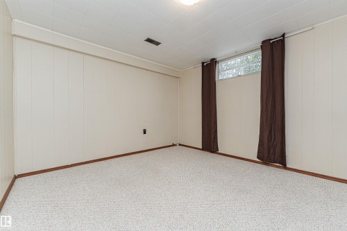 Carpeted room featuring light-colored panel walls, a drop ceiling, brown curtain panels, and a high horizontal window - 11423 50 Avenue, Edmonton, AB - Indoor Photo Showing Other Room