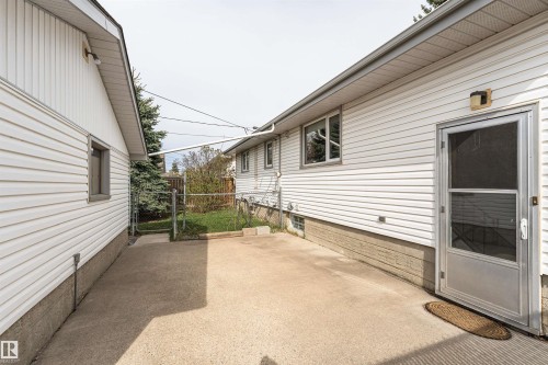 Concrete patio area between two structures, featuring white horizontal siding, a side entry door with a screen, and a chain-link fence - 11423 50 Avenue, Edmonton, AB - Outdoor With Exterior