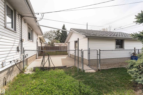 Chain-link fenced yard space featuring a concrete patio, a detached structure with vinyl siding, and a small grassy area - 11423 50 Avenue, Edmonton, AB - Outdoor With Deck Patio Veranda With Exterior