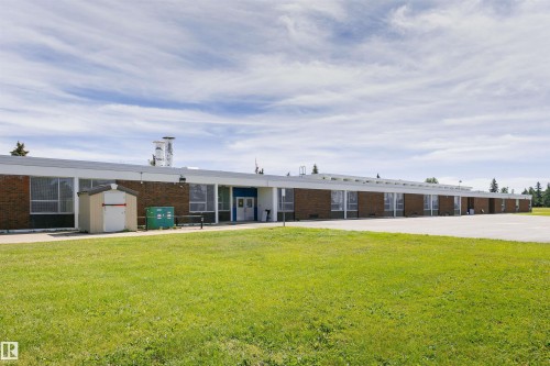 Brick and white facade building with multiple windows, a prominent entrance, and an expansive paved area - 11423 50 Avenue, Edmonton, AB - Outdoor