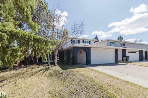 Exterior featuring a two-car garage with a white door, an arched entryway, dark siding accents, and light-colored upper-level siding - 10423 35 Avenue, Edmonton, AB - Outdoor With Facade
