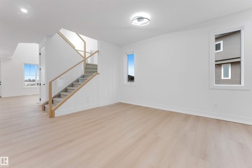 Living space featuring light-toned flooring, white walls, and a staircase with glass paneling and wooden handrails - 4004 35 Street, Beaumont, AB - Indoor Photo Showing Other Room