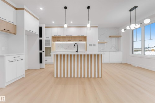 Modern kitchen featuring a central island with a sink and pendant lighting, white cabinetry with wood accents, and light wood flooring - 4004 35 Street, Beaumont, AB - Indoor Photo Showing Kitchen