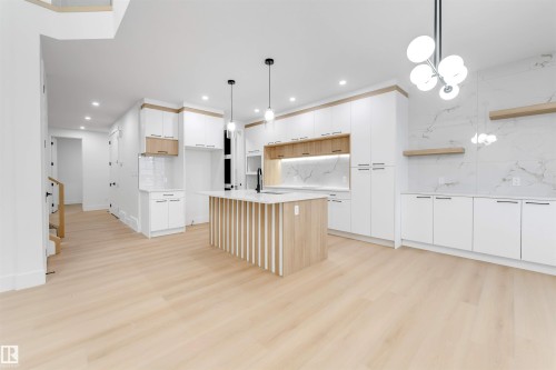 The spacious open-concept living area features light wood flooring, a kitchen island with a light wood base and white countertop, and white cabinetry with light wood accents - 4004 35 Street, Beaumont, AB - Indoor Photo Showing Kitchen
