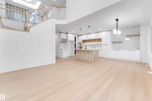 Expansive open concept living area featuring light-toned flooring, a modern kitchen with a center island, white cabinetry, and a marbled backsplash, and a staircase with glass panel railing - 4004 35 Street, Beaumont, AB - Indoor Photo Showing Kitchen