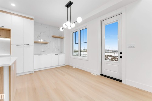The property features light wood flooring, a modern chandelier, and a white door with a window providing outdoor views - 4004 35 Street, Beaumont, AB - Indoor Photo Showing Other Room