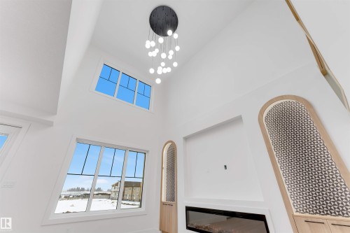 The living area features high vaulted ceilings, expansive windows, a sleek linear fireplace, and unique built-in shelving with decorative paneling - 4004 35 Street, Beaumont, AB - Indoor Photo Showing Other Room