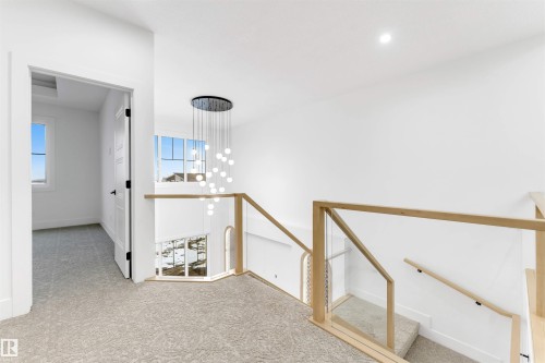 The property features a contemporary staircase with glass railings and light wood handrails, illuminated by a striking modern chandelier - 4004 35 Street, Beaumont, AB - Indoor Photo Showing Other Room