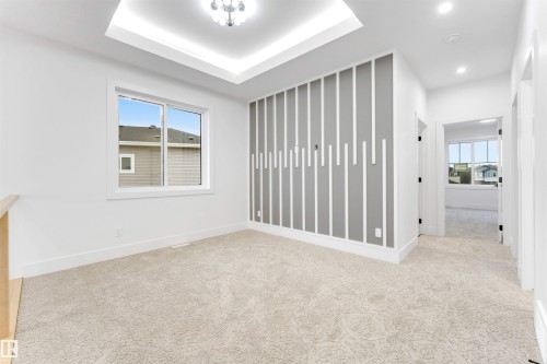 This bright room features a decorative accent wall, a window providing natural light, and plush carpet flooring, complemented by a tray ceiling with an overhead light fixture - 4004 35 Street, Beaumont, AB - Indoor Photo Showing Other Room